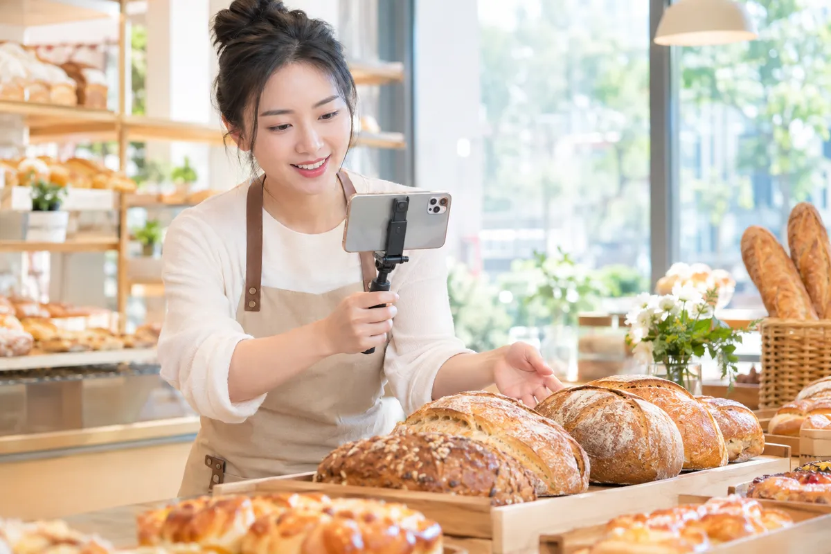 烘焙店老板在柜台前用手机拍摄新鲜面包